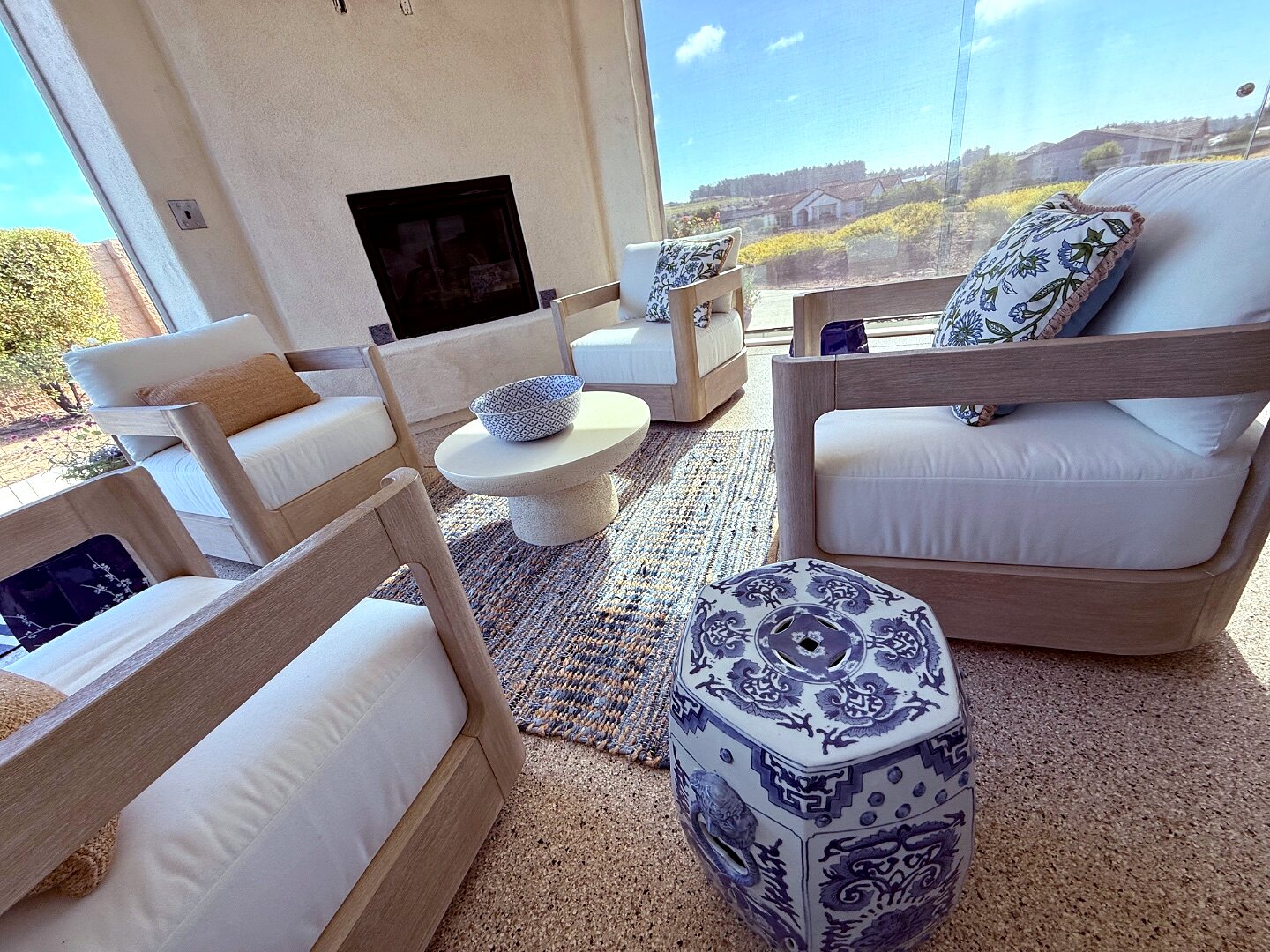 Sunroom with light-wood armchairs, a blue-and-white garden stool, and the view through glass doors to the landscape beyond