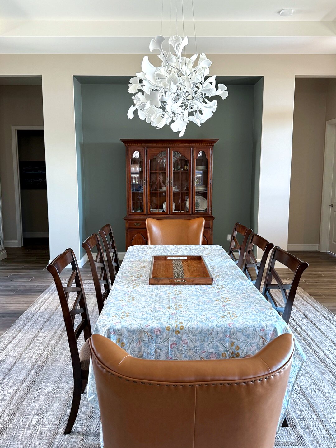 Dining room after — a feminine space with a floral tablecloth, cognac host chair, and a sculptural white chandelier