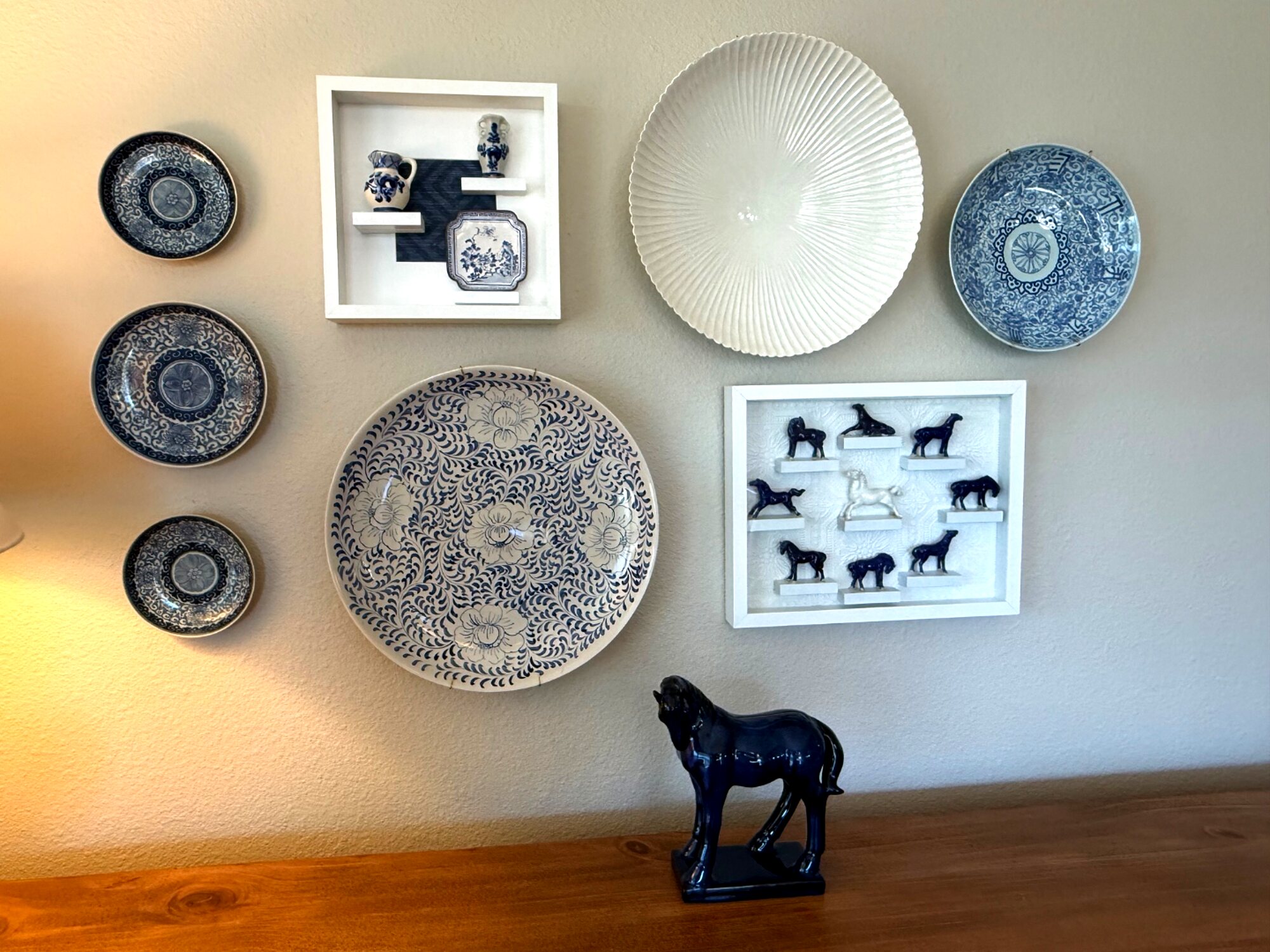 Gallery wall of blue-and-white plates and shadow boxes with miniature vessels above a sideboard
